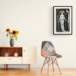 May include: An Art Deco style framed print featuring a woman in an elaborate gown with a bird. The print is in a black frame and hangs on a white wall. A modern cabinet with a vase of sunflowers and a patchwork chair are in the foreground.