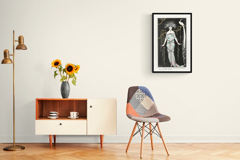 May include: An Art Deco style framed print featuring a woman in an elaborate gown with a bird. The print is in a black frame and hangs on a white wall. A modern cabinet with a vase of sunflowers and a patchwork chair are in the foreground.