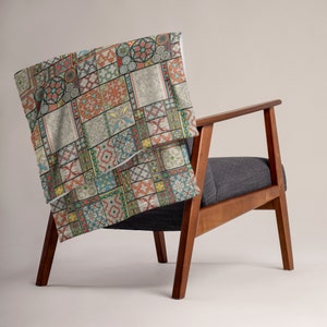 May include: A colourful throw blanket with a geometric pattern featuring various shades of red, blue, green, yellow, and white. The blanket is draped over a wooden armchair with a grey fabric seat.