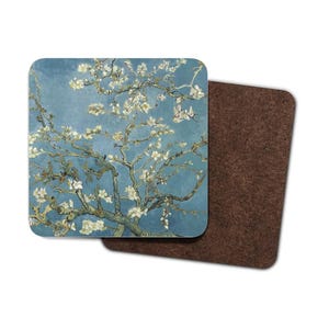 Può includere: Un sottobicchiere quadrato con un dipinto di un mandorlo in fiore con fiori bianchi su uno sfondo di cielo blu. Il sottobicchiere ha un retro in sughero.