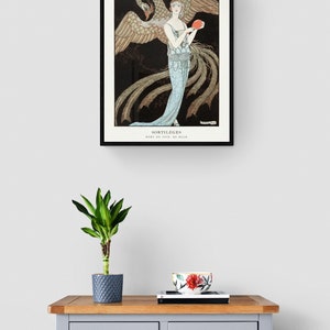 May include: A framed art print featuring a woman in a flowing blue gown holding a red object, with a large bird behind her. The print is titled "SORTILEGES" and is displayed above a gray dresser with a plant and decorative bowl.