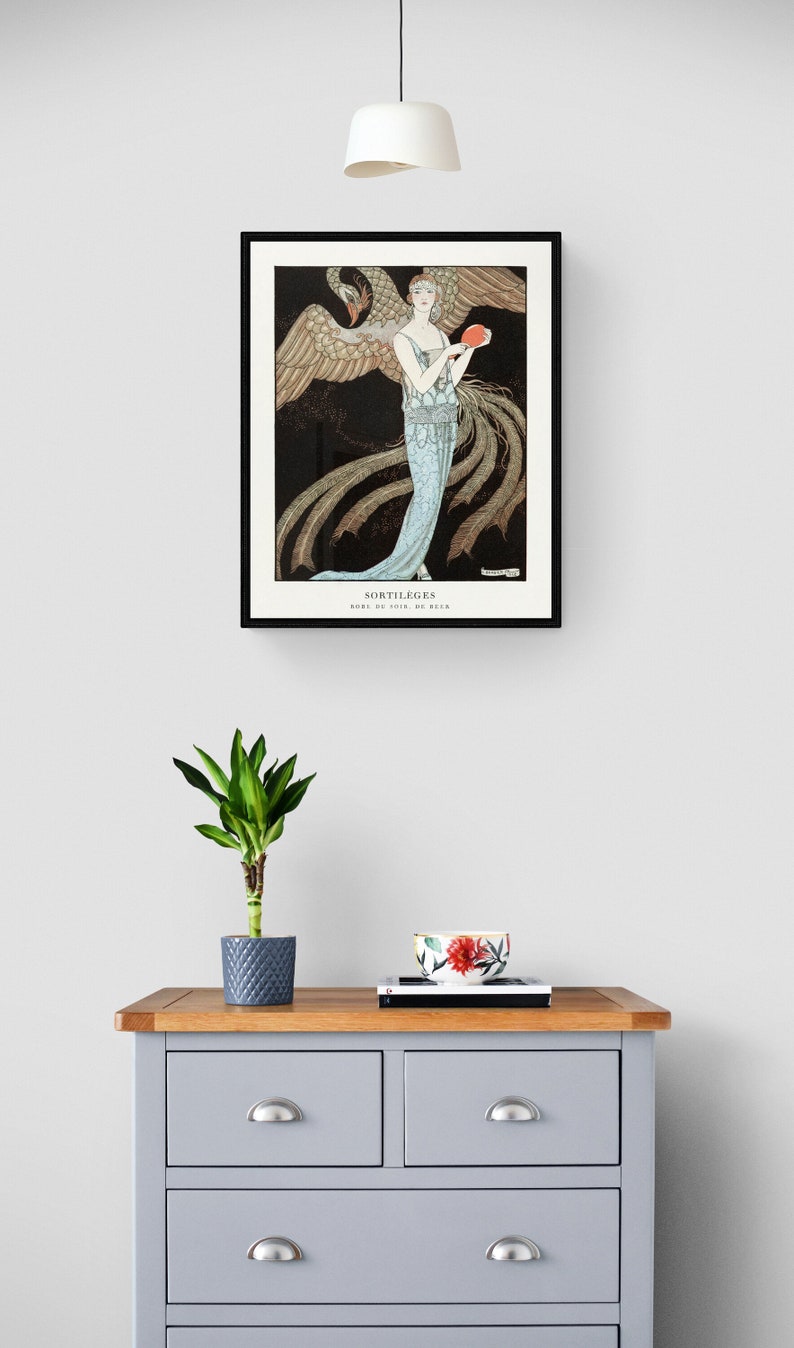 May include: A framed art print featuring a woman in a flowing blue gown holding a red object, with a large bird behind her. The print is titled "SORTILEGES" and is displayed above a gray dresser with a plant and decorative bowl.