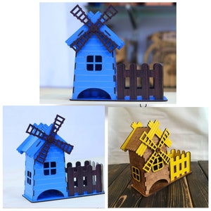 May include: Wooden windmill desk organizer in blue and brown. The windmill features a blue body, brown blades, and a small fence. The design is a decorative and functional item for a desk or shelf.