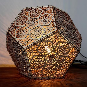 May include: A wooden geometric lampshade with a intricate laser-cut design. The lampshade is illuminated from within, casting a warm glow.
