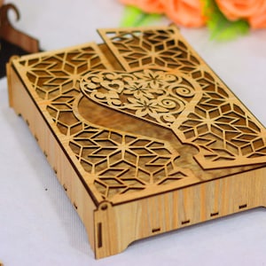 Puede incluir: Una caja de madera con una tapa con bisagras. La tapa tiene un diseño recortado de un corazón con detalles intrincados. La caja está hecha de madera marrón claro y tiene un acabado de madera natural.