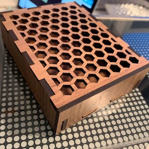 May include: A small wooden box with a honeycomb pattern cut out of the top. The box is made of dark wood with a light wood interior.