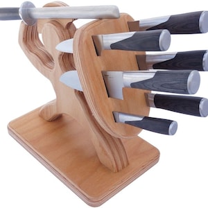 Op de afbeelding: Een houten messenblok in de vorm van een persoon die een zwaard en schild vasthoudt. De messenblok heeft gleuven voor zes messen en een slijpstaal.