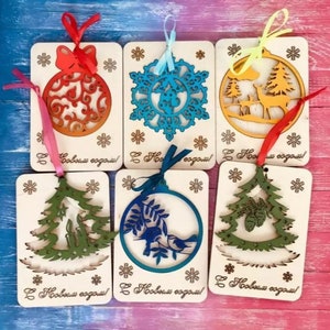 Può includere: Sei ornamenti natalizi in legno con diversi design, tra cui un fiocco di neve, un albero di Natale, un cervo in un bosco e un uccello su un ramo. Ogni ornamento è dipinto in un colore diverso, tra cui blu, verde, arancione e giallo. Gli ornamenti sono attaccati a una corda e hanno il testo "С Новым годом!" scritto su di essi.