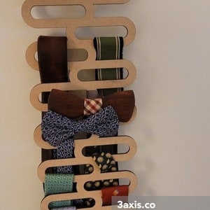 May include: A wooden tie rack with a unique design, featuring multiple slots to hold ties and bow ties. The rack is made of light brown wood and has a natural finish. It is mounted on a white wall and is filled with a variety of colorful ties and bow ties.