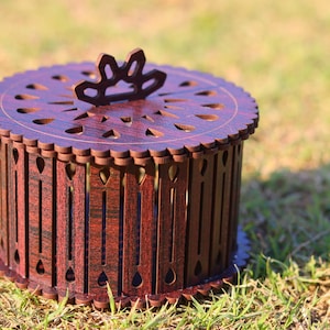 May include: A round wooden box with a decorative top and a lattice design. The box is made of dark wood with a reddish brown finish.