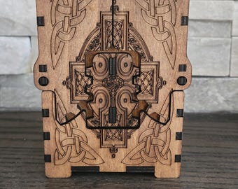 May include: A wooden box with a Celtic knot design. The box is made of light brown wood and features intricate carvings of interwoven patterns. The box is rectangular with a hinged lid and a latch closure. The design is symmetrical and detailed.