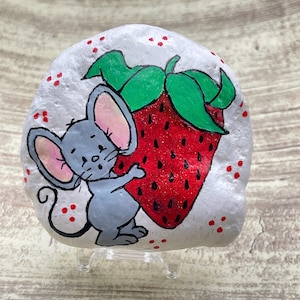 Topolino stravagante che tiene in mano una grande roccia dipinta a forma di fragola rossa glitterata, simpatica pietra da giardino a forma di animale, regalo per gli amanti delle fragole
