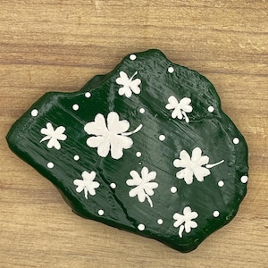 Puede incluir: Una roca pintada de verde con diseños de trébol de cuatro hojas blancos y puntos blancos.