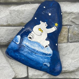 Adorable oso polar de invierno sentado sobre un iceberg que pone estrellas en el cielo nocturno, decoración de invierno, piedra pintada