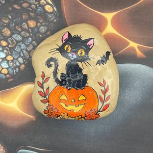 Schattige zwarte kat zittend op pompoen, herfst Halloween-decoratie, geschilderde rots, steenschildering