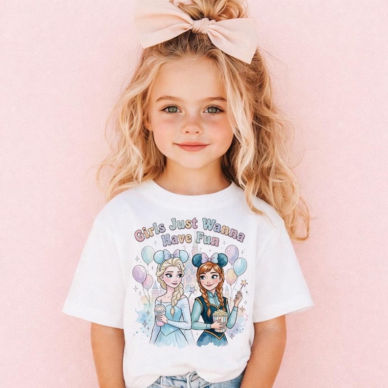 A young girl with blonde hair wearing a white t-shirt with a graphic of two cartoon girls and the text "Girls Just Wanna Have Fun" printed on it.