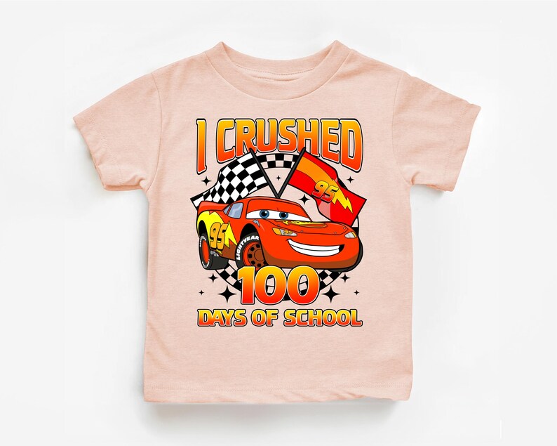 A pink t-shirt with a graphic design featuring a cartoon car and the text "I CRUSHED 100 DAYS OF SCHOOL".