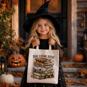 May include: A cream-colored canvas tote bag featuring a graphic print of a stack of five books with Halloween-themed illustrations. The text READ, SCREAM, REPEAT is printed in black above the books, which are decorated with pumpkins, cats, and moons.