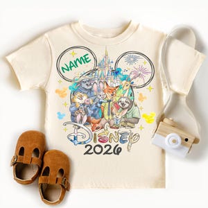 A Disney-themed t-shirt with a group of cartoon characters, a pair of brown baby shoes, and a camera.
