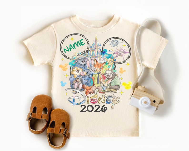 A Disney-themed t-shirt with a group of cartoon characters, a pair of brown baby shoes, and a camera.