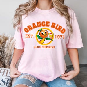 a woman wearing a pink shirt with an orange bird on it