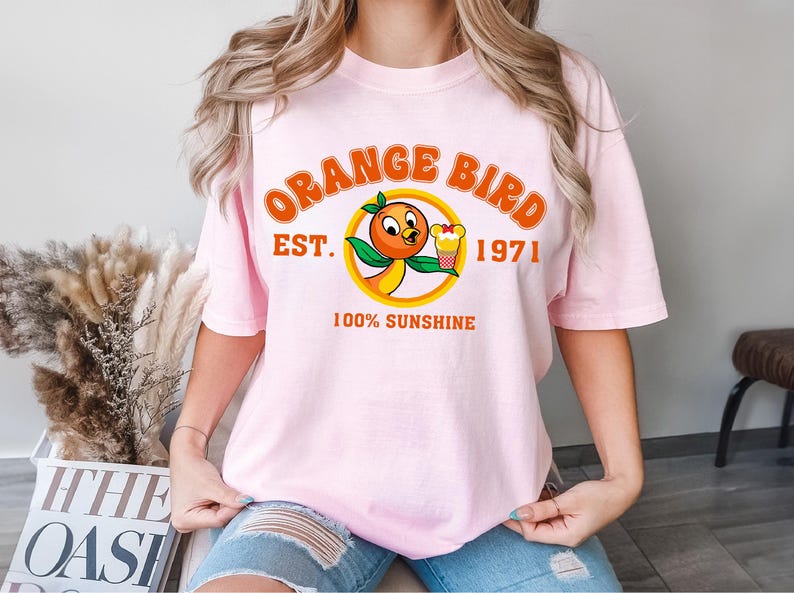 a woman wearing a pink shirt with an orange bird on it
