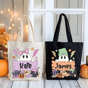May include: Two Halloween-themed tote bags. One is cream-colored, the other black. Each features a cartoon ghost holding a sign with a name, surrounded by Halloween graphics, including pumpkins, candy, and a cauldron. The cream bag says "Kate". The black bag says "James".