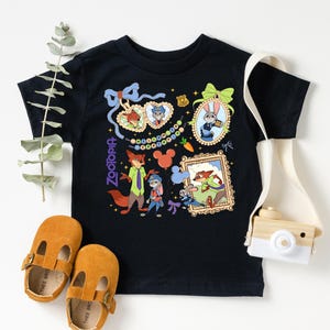 a black t-shirt with a colorful graphic design, a pair of brown baby shoes, and a white camera.