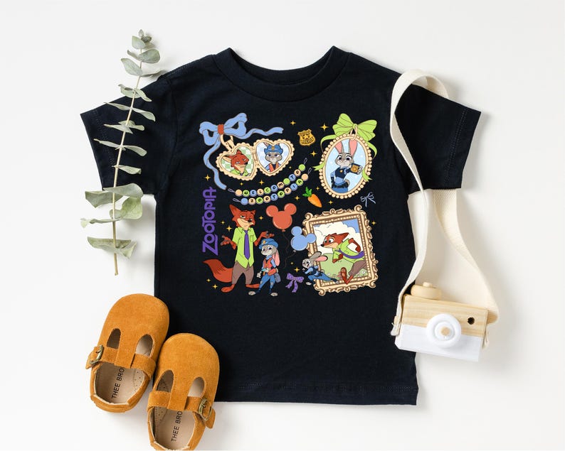 a black t-shirt with a colorful graphic design, a pair of brown baby shoes, and a white camera.