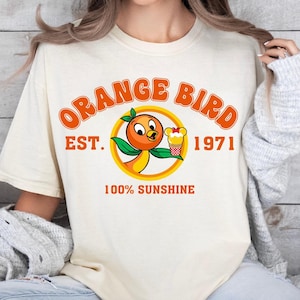 a woman sitting on a bed wearing an orange bird t - shirt