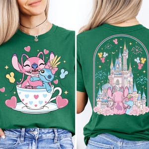 A green t-shirt with a cartoon image of two pink characters, one inside a teacup and the other on a castle, surrounded by hearts and fireworks.