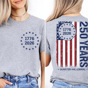 a woman wearing a grey t-shirt with a graphic design on the back. The design includes a circle with the numbers 1776 and 2026, and an American flag pattern.