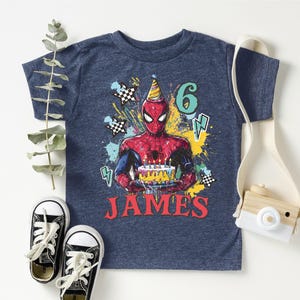 A blue t-shirt with a Spider-Man graphic and the number 6, along with a pair of sneakers and a camera, all arranged on a white background.