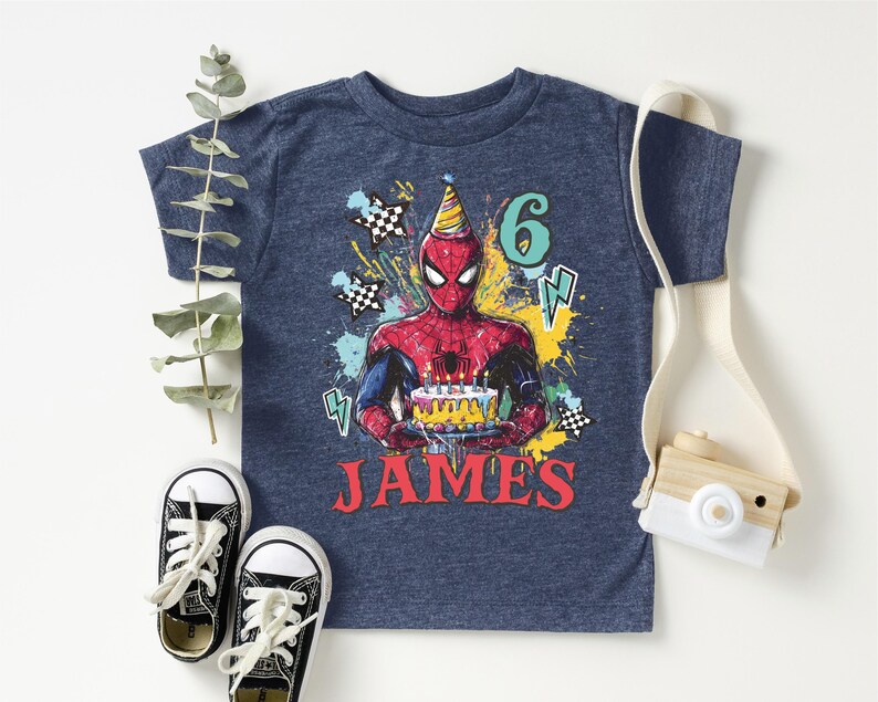 A blue t-shirt with a Spider-Man graphic and the number 6, along with a pair of sneakers and a camera, all arranged on a white background.