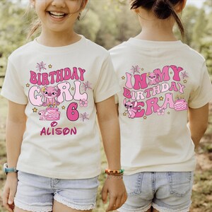 A young girl wearing a white t-shirt with a birthday design and text on the back.