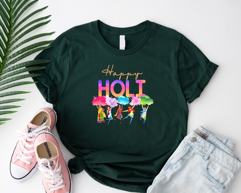May include: A dark green t-shirt with the text 'Happy Holi' in rainbow colors. The t-shirt has a graphic of people celebrating Holi with colorful powder.