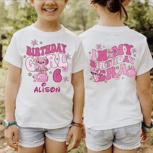 A young girl wearing a white t-shirt with a birthday design and text on it, standing in a grassy field.