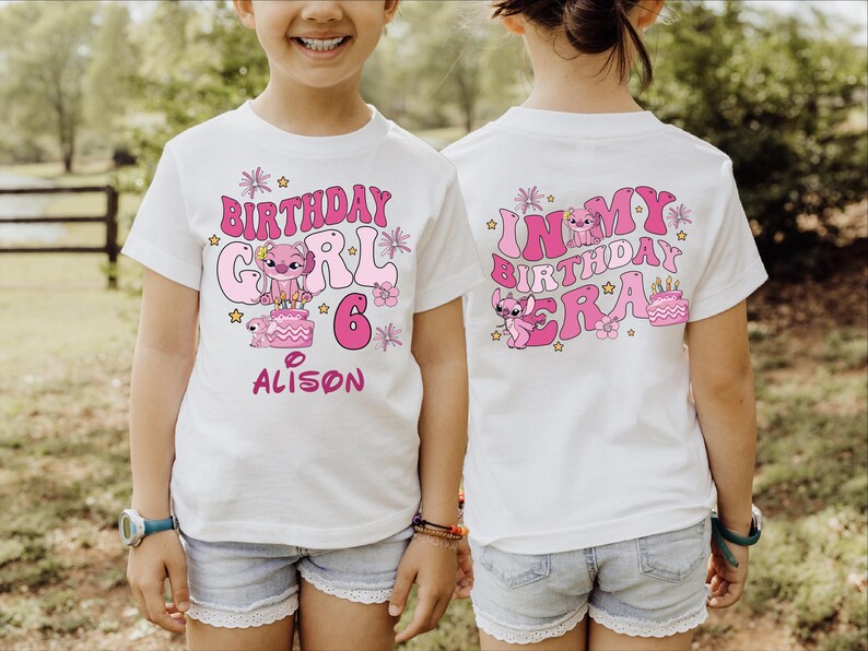 A young girl wearing a white t-shirt with a birthday design and text on it, standing in a grassy field.