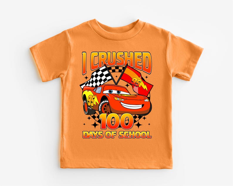 An orange t-shirt with a graphic design featuring a cartoon car and the text "I CRushed 100 DAYS OF SCHOOL".