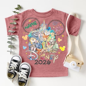 A pink Disney-themed t-shirt with various Disney characters, a pair of black and white sneakers, and a camera, all arranged on a white background.