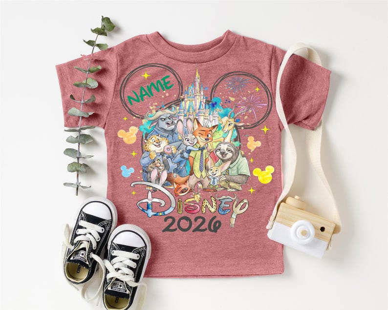 A pink Disney-themed t-shirt with various Disney characters, a pair of black and white sneakers, and a camera, all arranged on a white background.