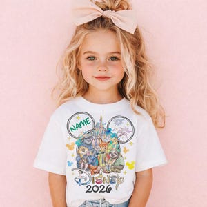 A young girl with blonde hair wearing a white t-shirt with a Disney-themed design and a pink bow on her head.