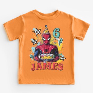 An orange t-shirt with a Spiderman graphic and the number 6, along with the text "JAMES" printed on it.