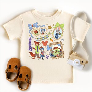 a white t-shirt with a cartoon character design, a pair of brown baby shoes, and a white camera.