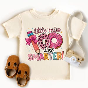 a white shirt with a pink donut and a pair of brown shoes