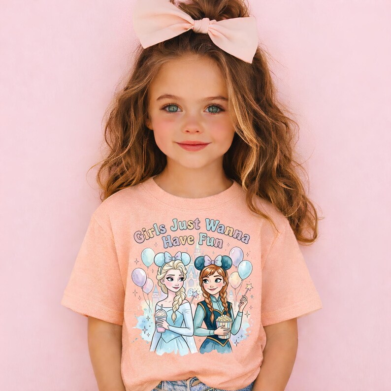A young girl with long brown hair wearing a pink bow and a pink t-shirt with a graphic of two cartoon girls.