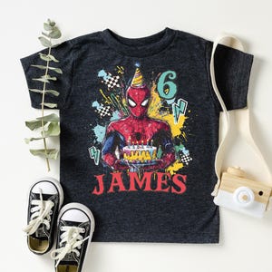A black t-shirt with a Spider-Man graphic and the number "6" printed on it, along with a pair of sneakers and a camera.