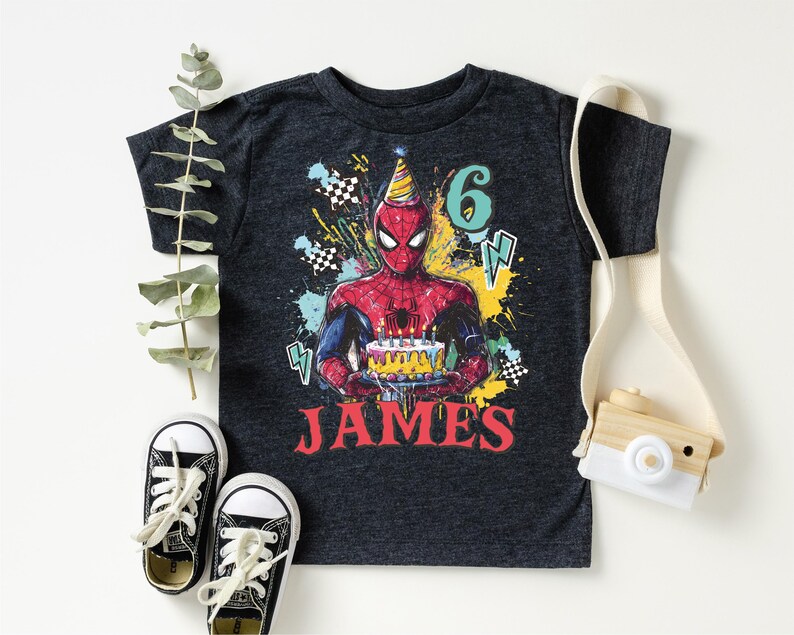 A black t-shirt with a Spider-Man graphic and the number "6" printed on it, along with a pair of sneakers and a camera.