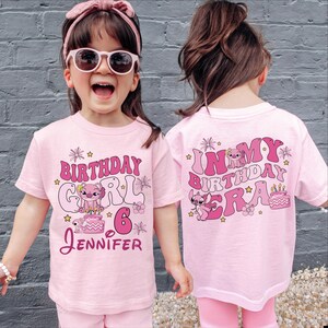 Two young girls wearing pink t-shirts with birthday messages and illustrations.