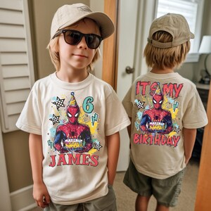 A young boy wearing a Spiderman-themed birthday t-shirt and a baseball cap, with a birthday celebration design on the back of his shirt.